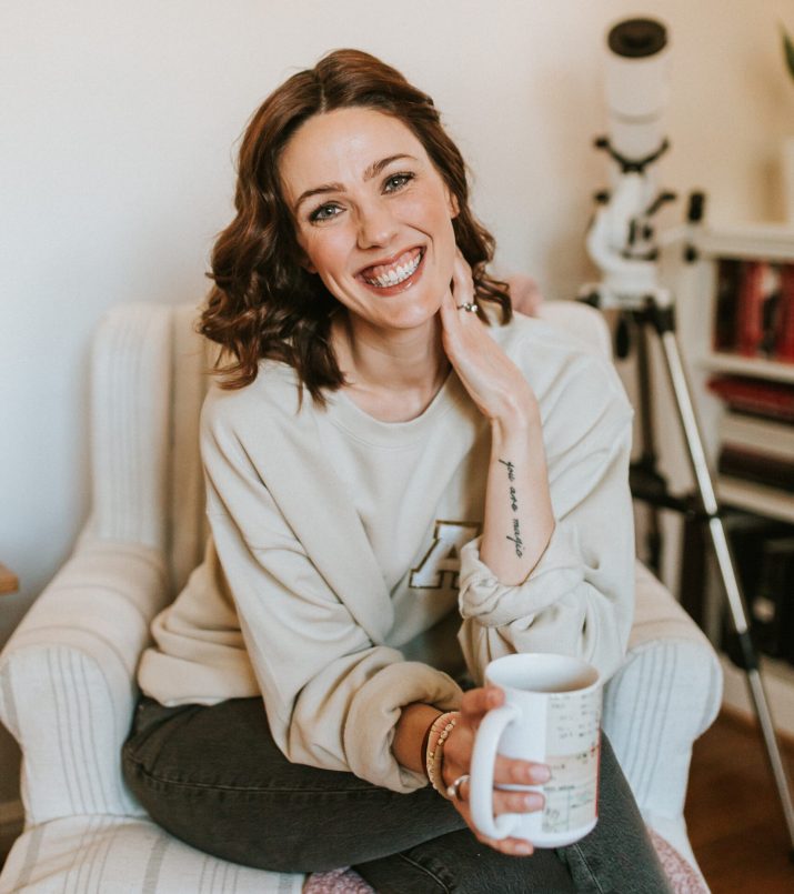 Woman sitting in a chair holding coffee and smiling Woman sitting in a chair holding coffee and smiling