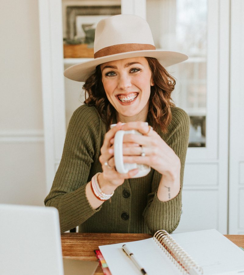 Woman wearing a hat and holding a coffee cup working at computer