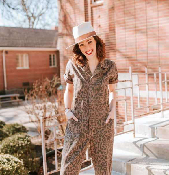 Woman wearing a hat, leopard jumpsuit, and red lipstick smiling at the camera